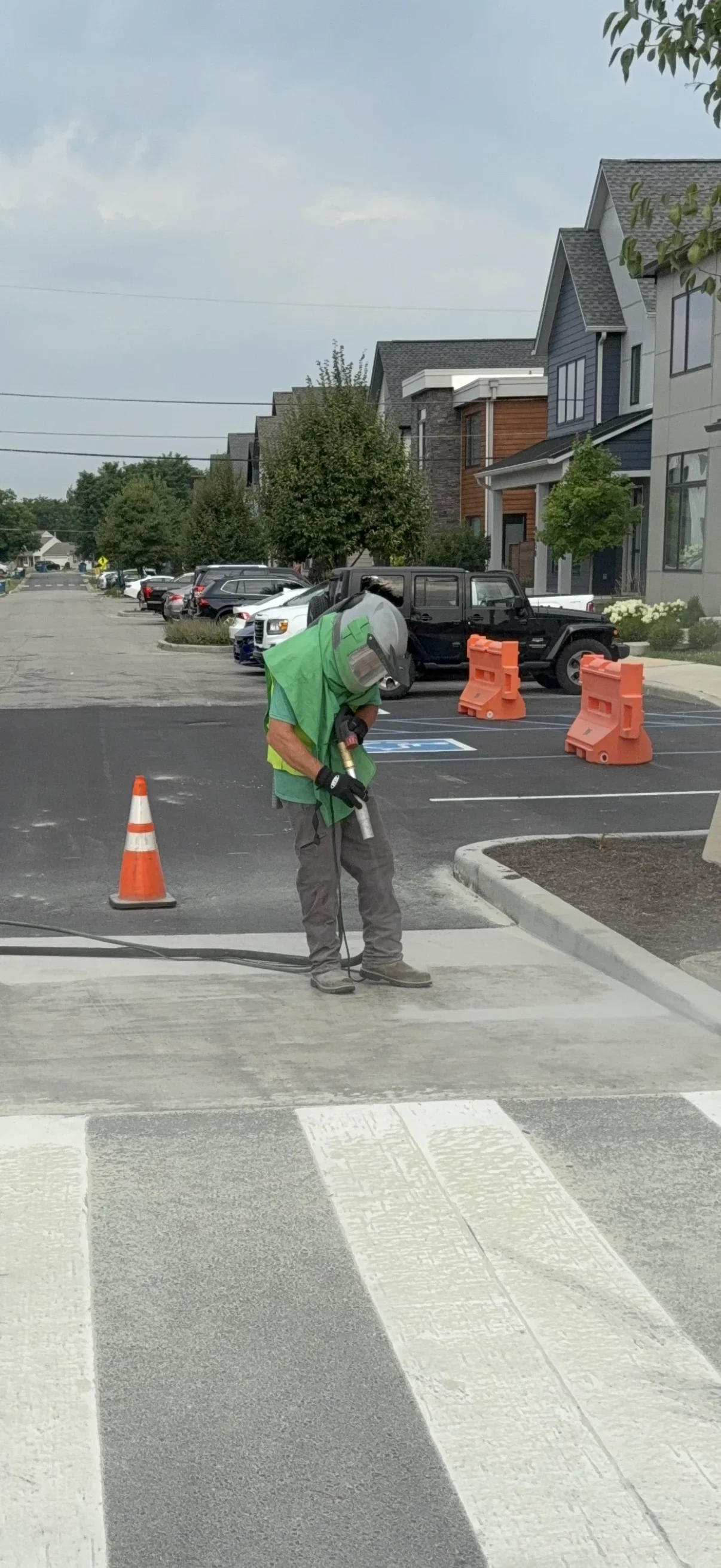 Worker operating sandblasting equipment on asphalt parking lot with safety cones and traffic barriers