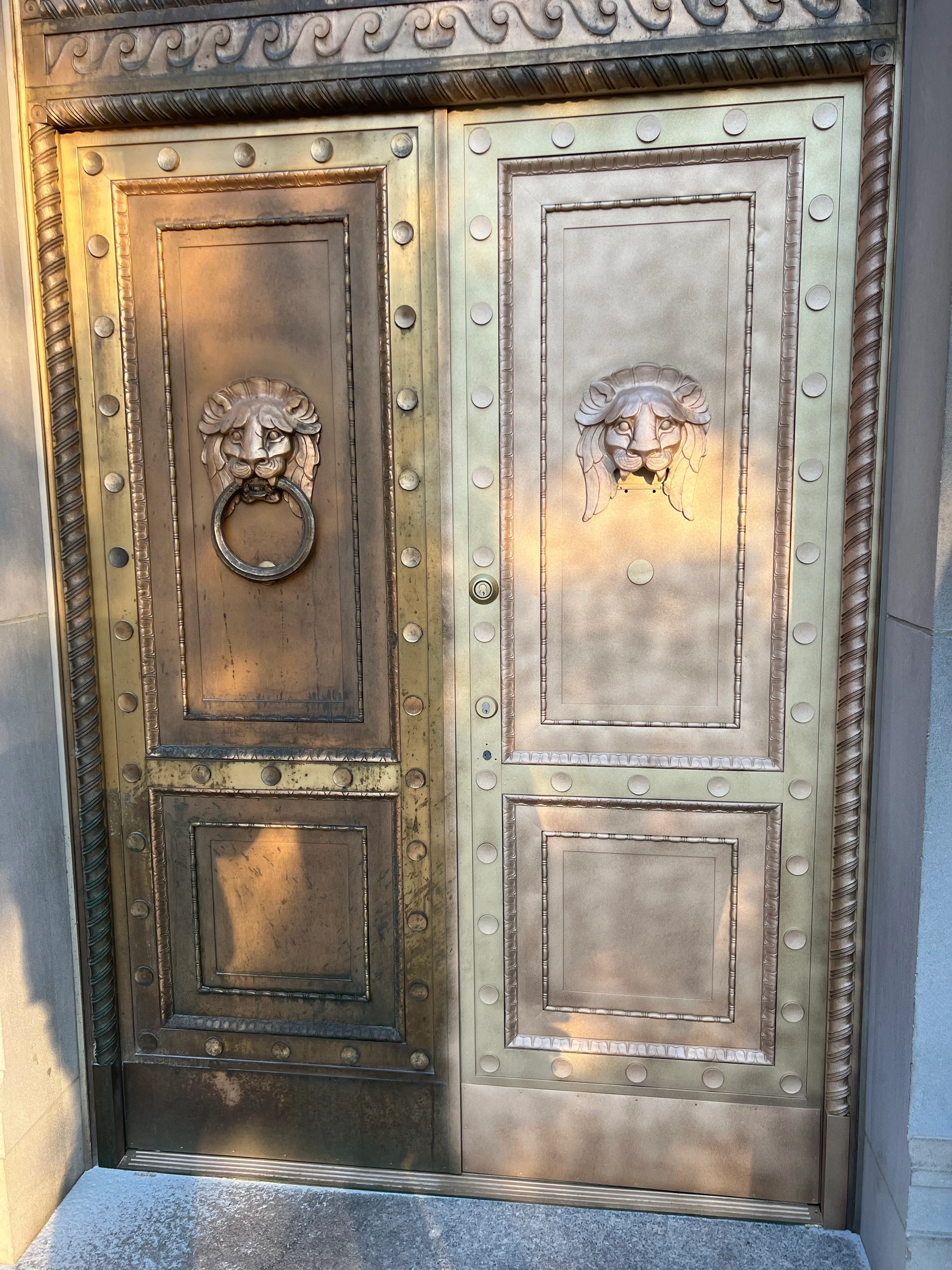 Restored bronze double doors with lion head knockers and decorative studs, showing cleaned metal finish