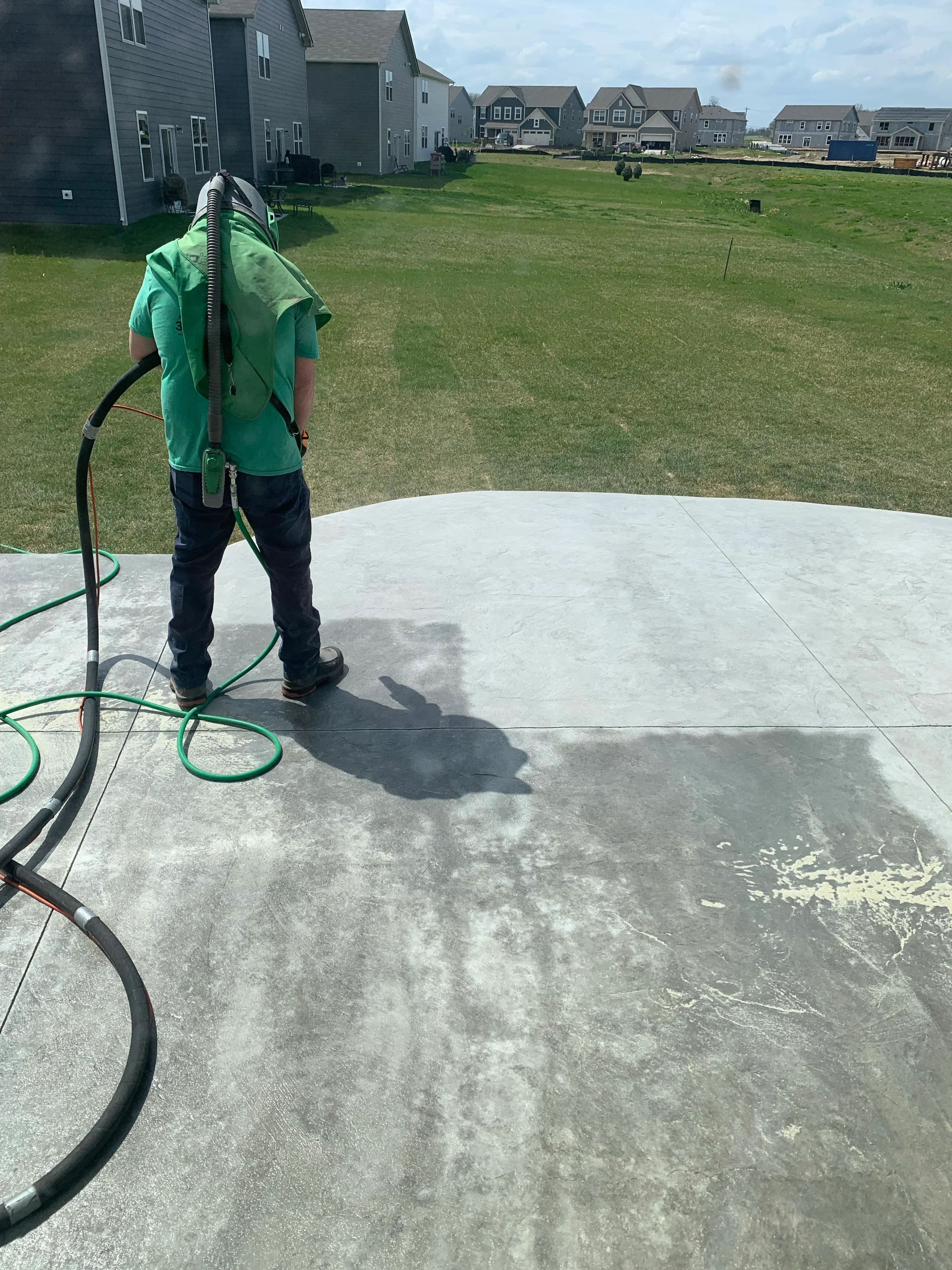 Technician pressure washing concrete pad with professional equipment and green hose