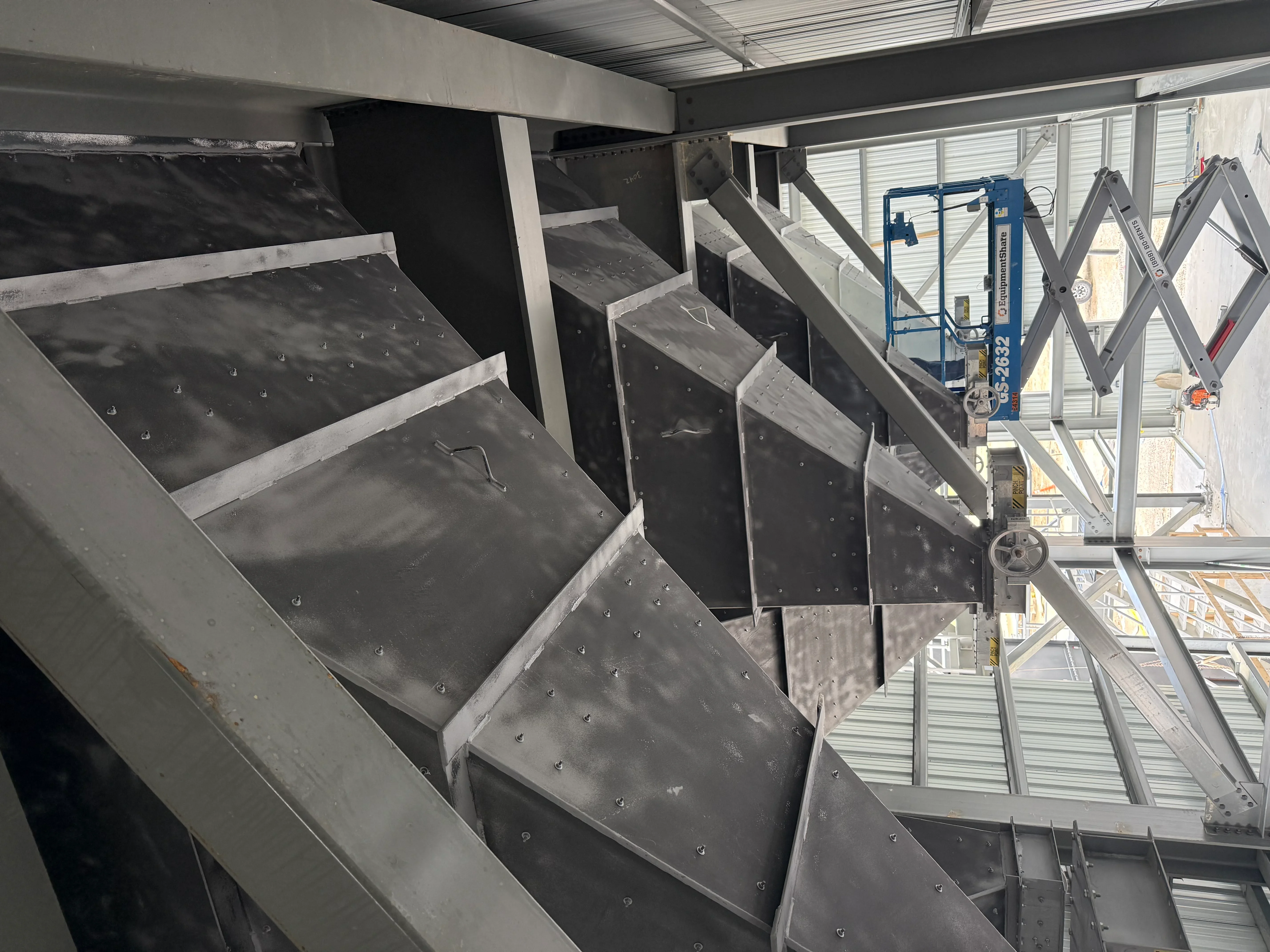 Sandblasted industrial metal equipment with riveted panels and angled surfaces in preparation bay