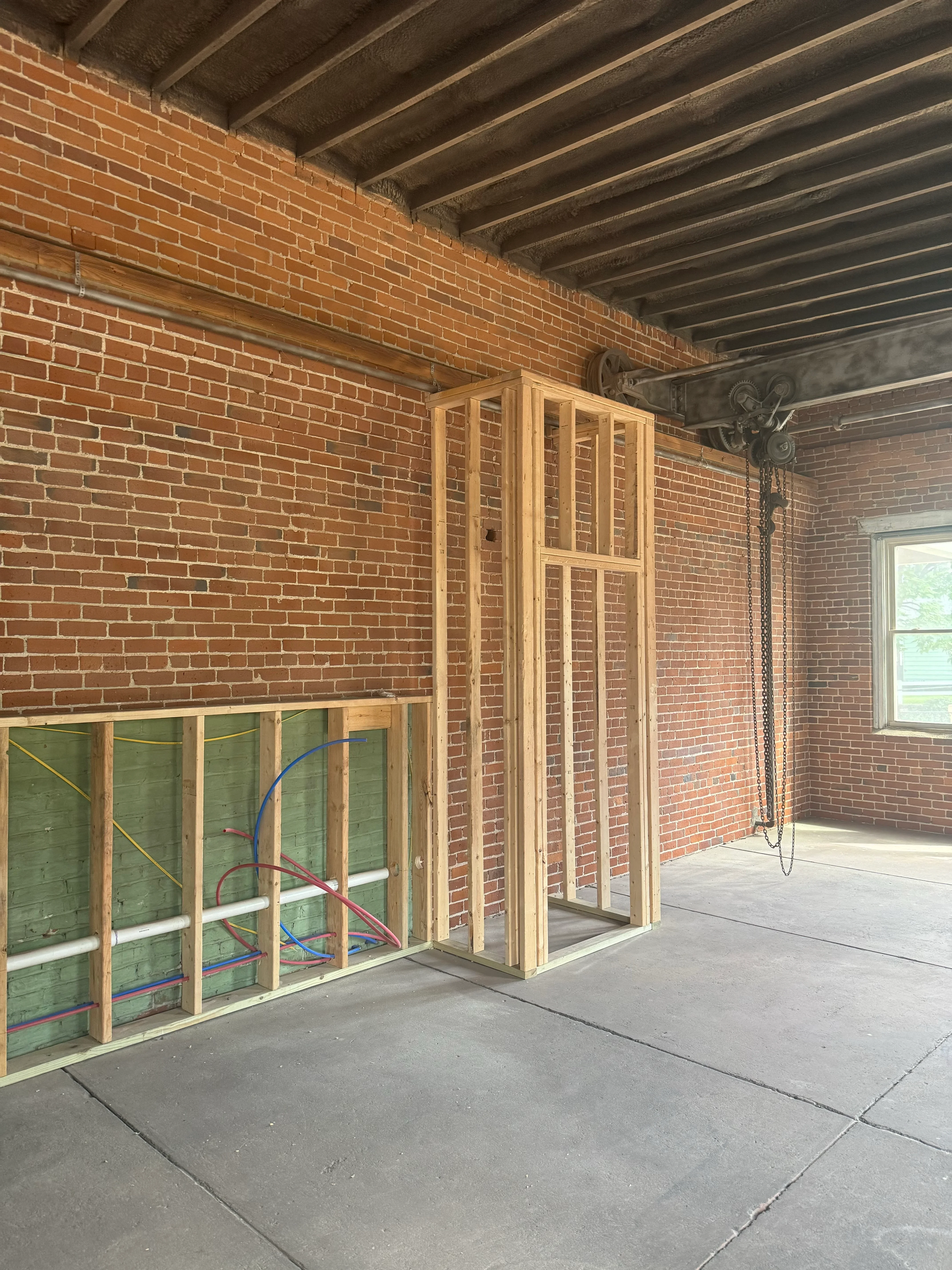 Red brick wall with wood framing studs and electrical conduit during interior renovation preparation