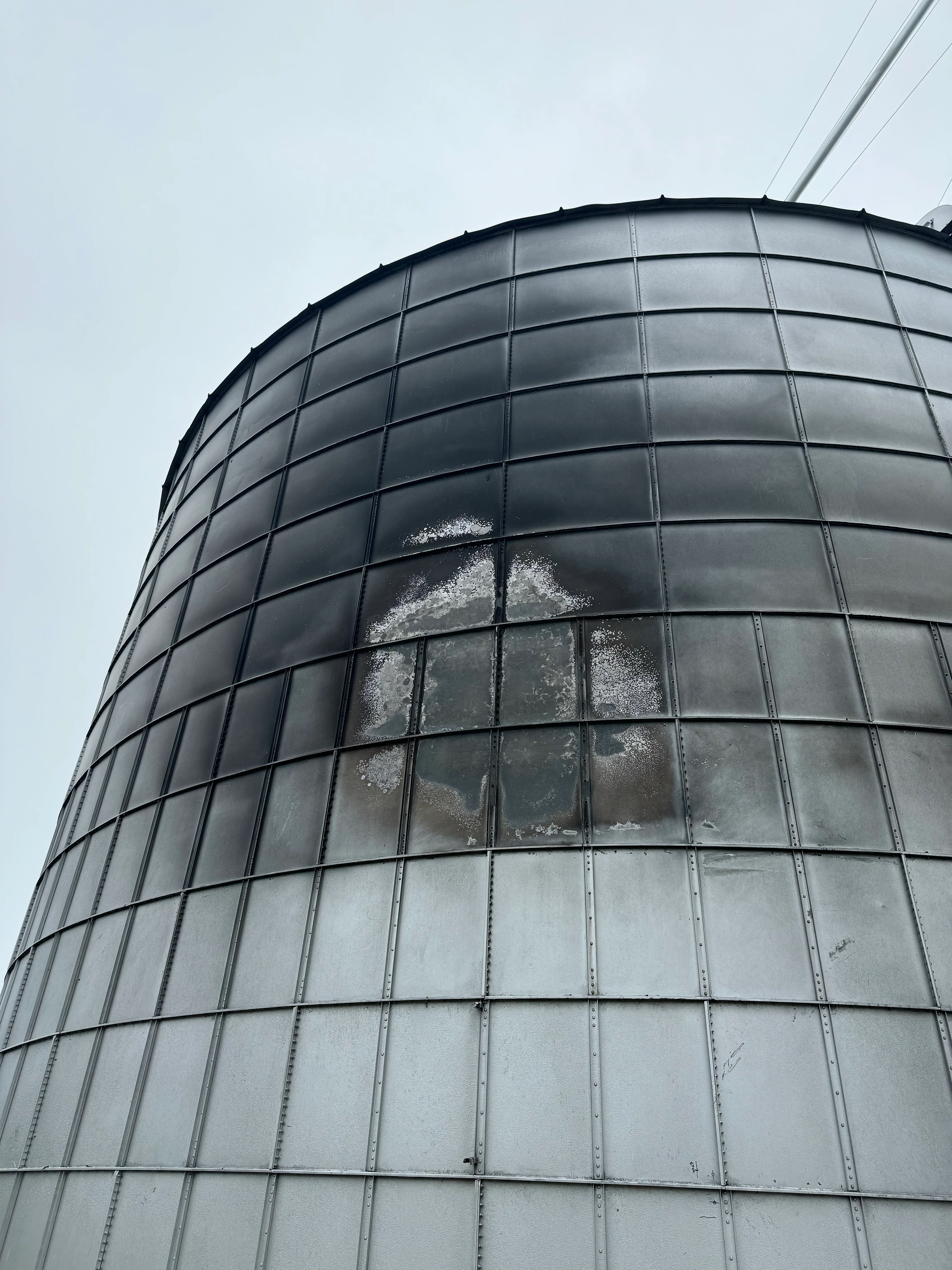 Cylindrical metal tank with sandblasted panels showing cleaned galvanized steel surface and grid framework