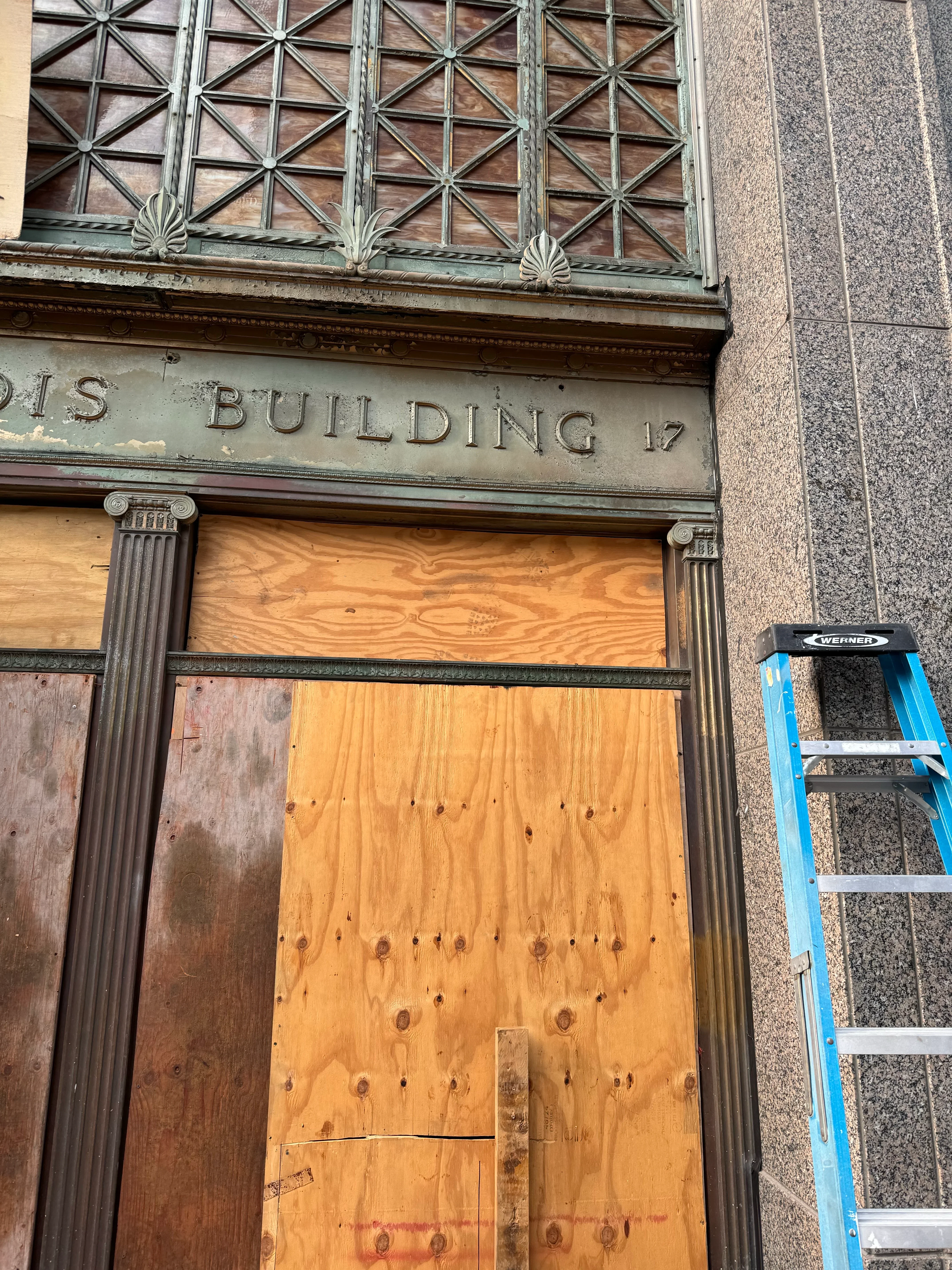 Historic building entrance with ornate cast iron grilles and stone facade during sandblasting restoration