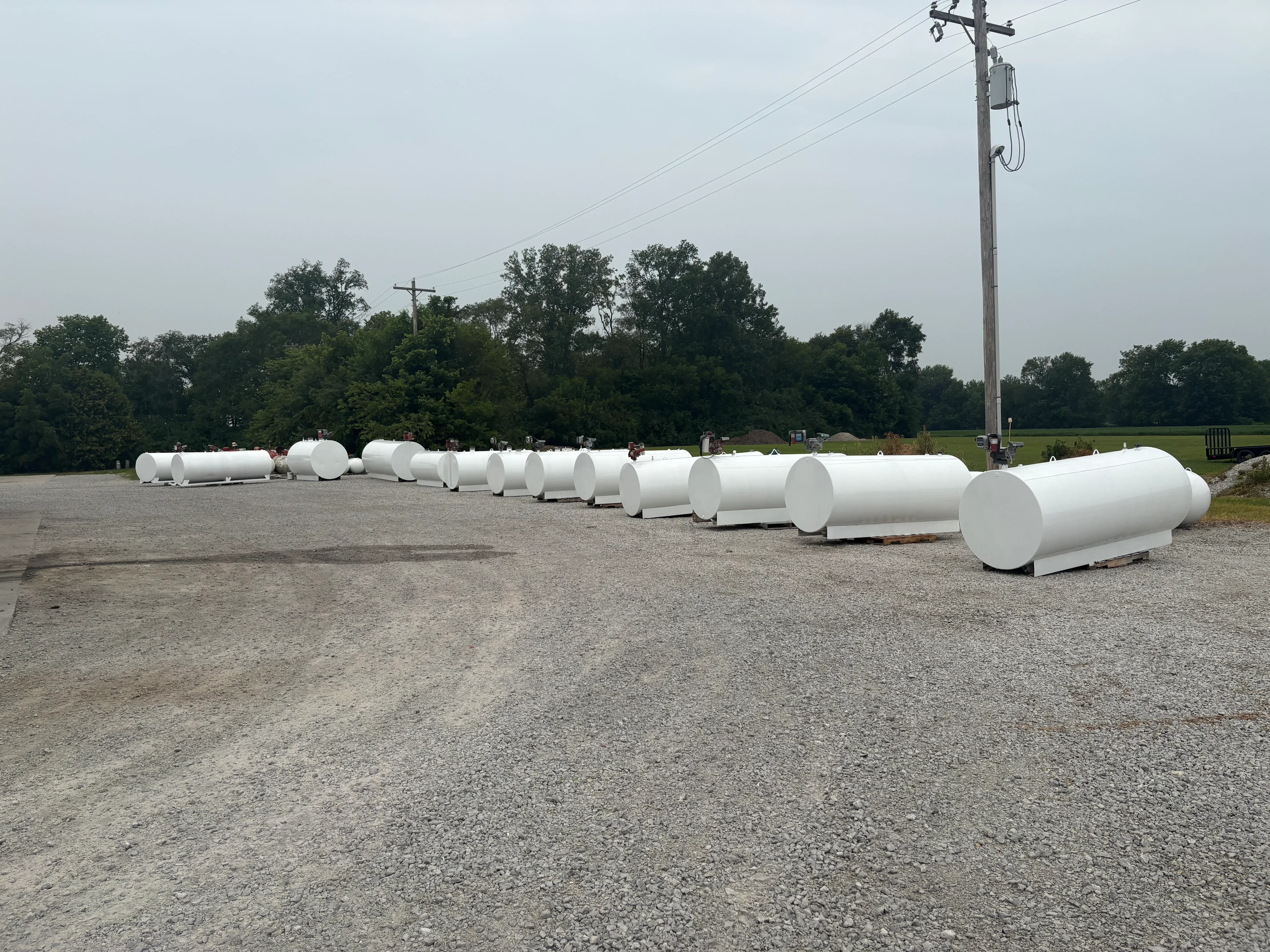 Row of white cylindrical propane tanks prepared with sandblasting on gravel surface