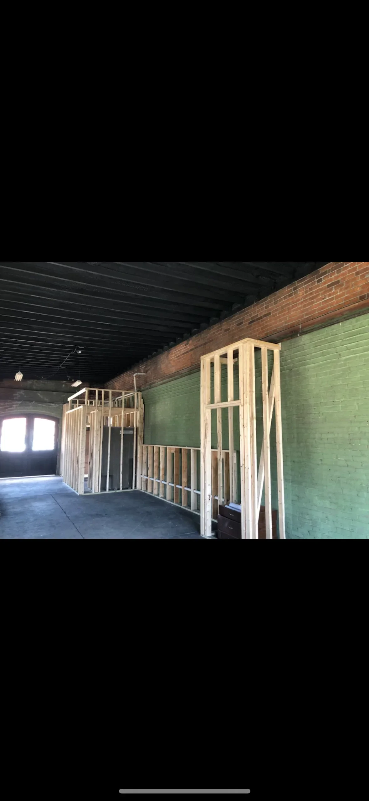 Green-primed brick wall with wooden framing studs and prepared concrete floor in industrial interior